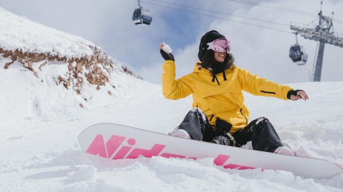 Girl on snowboard sitting on slope throwing snowball