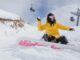 Girl on snowboard sitting on slope throwing snowball