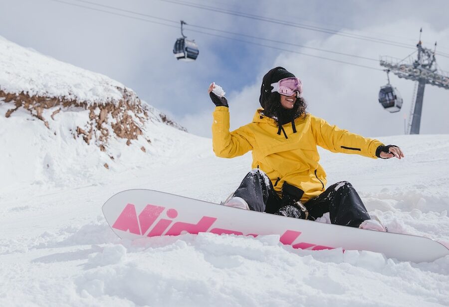 Girl on snowboard sitting on slope throwing snowball